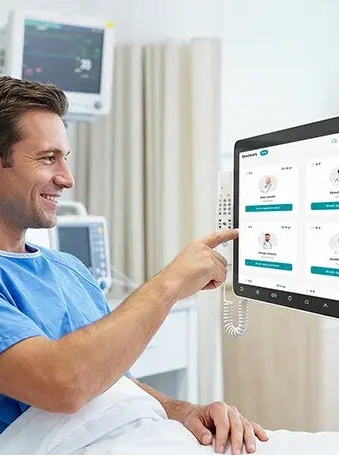 Person in a hospital bed using a Hitekon Patient Infotainment Terminal with a healthcare interface.